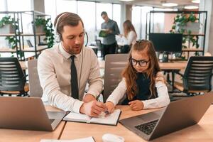 Man is, helping, teaching. Little girl is in the office where people working together photo