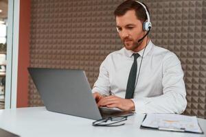 Using, laptop. Handsome man in formal clothes is in the office photo