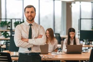 Man in tie is ,standing in front of his colleagues. Business people in formal clothes are working in the office together photo