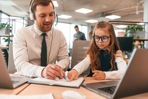 Man is helping, teaching. Little, girl is, in the office where people working together photo