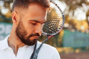 Standing, with racket in hands. Young man is on the tennis court at sunny daytime photo