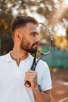 Standing, with racket in hands. Young man is ,on the tennis court at sunny daytime photo