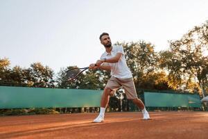 Active, training. Young man is on the tennis court at sunny daytime photo