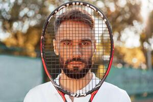Standing with racket in hands. Young man is, on the tennis court at sunny daytime photo