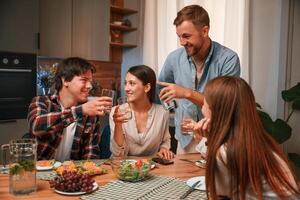 Holding glasses with, water. Group of people are on the kitchen, having dinner, spending time together photo