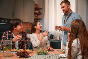 Holding ,glasses with water. Group of people are on the kitchen, having dinner, spending time together photo