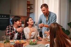 Holding glasses with water.. Group of people are on the kitchen, having dinner, spending time together photo