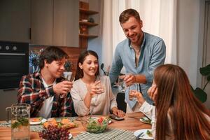 Holding, glasses with water. Group of people are on the kitchen, having dinner, spending time together photo