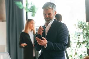 Senior man ,is standing in front of colleagues. Group of business people are working in the modern office photo
