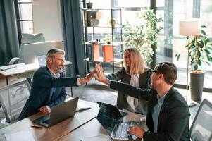 Making high, five, sitting by the table. Group of business people are working in the modern office photo