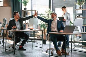 Men are giving high five. Group of business people are working in the modern office photo