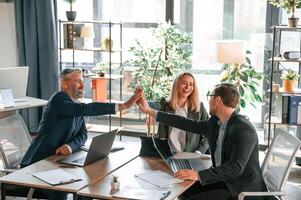 Making high five, sitting, by the table. Group of business people are working in the modern office photo