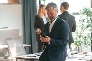 Senior man is standing in, front of colleagues. Group of business people are working in the modern office photo