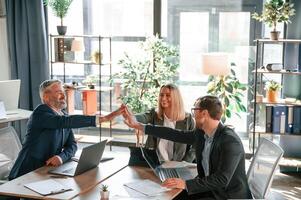 Making high,, five, sitting by the table. Group of business people are working in the modern office photo