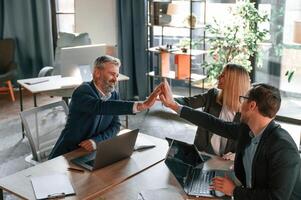 Making high, five, sitting by ,the table. Group of business people are working in the modern office photo