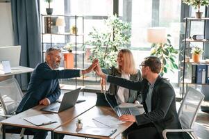 Making high five,, sitting by the table. Group of business people are working in the modern office photo
