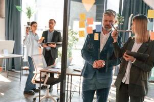 Conception of plan. Many stickers are on the glass. Group of business people are working in the modern office photo