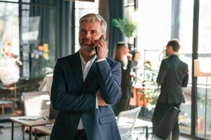 Man is standing and having phone call. Group, of, business people are working in the modern office photo