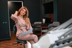Sitting and holding document., Beautiful ,young female doctor is indoors in the cabinet photo