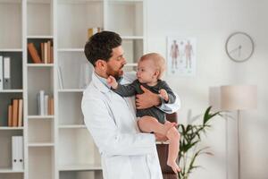Standing, and holding boy. Doctor, with little baby is working in the cabinet photo