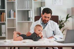 With ,stethoscope. .Doctor with little baby is working in the cabinet photo