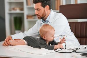 With stethoscope.. Doctor with little baby is working in the cabinet photo