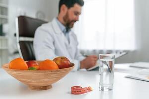 Fruits is on the table. Doctor ,in formal clothes is working in the cabinet photo