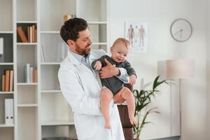 Standing and holding boy. Doctor with little, baby is working in the cabinet photo
