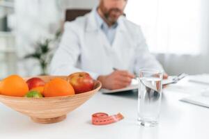 Fruits is on the table. Doctor in formal clothes is working in the cabinet photo