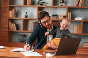 Conception, of multitasks. Businessman in formal clothes is working indoors. With toddler photo