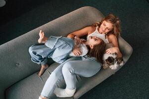 Lying down on the sofa. Mother with her daughter and with cute dog is in domestic room photo