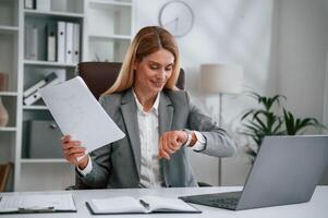 Checking, the time, holding document. Woman in business formal clothes is working in office photo