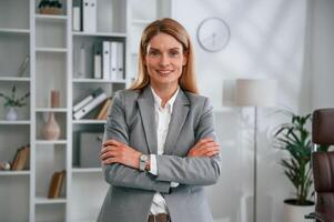Standing with arms crossed. Woman in business formal clothes is working in office photo