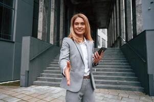 Giving ,greeting ,hand. Woman in formal clothes is outdoors near the business building photo
