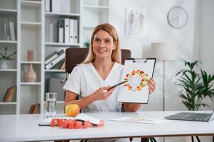 With picture of food and vitamins.. Young female doctor in white coat is indoors photo