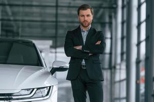 Man ,in black suit is indoors in the car dealership near automobile photo