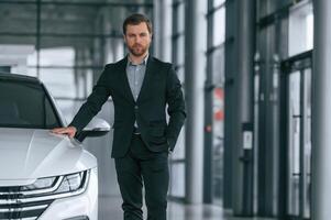 Man, in black suit is indoors in the car dealership near automobile photo
