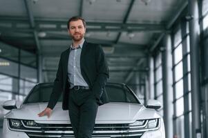 Man in, black suit is indoors in the car dealership near automobile photo