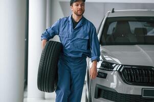 With tire in the hands. .Man in blue uniform is working in the car service photo