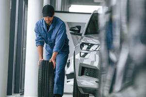 Moving the ,tire. Man in blue uniform is working in the car service photo