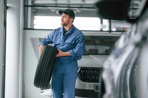 With tire ,in the hands. Man in blue ,uniform is working in the car service photo