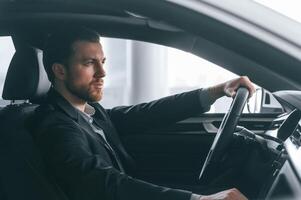 Serious facial expression. Driving the, car. Man in formal business clothes is sitting in the modern automobile photo