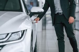 Close up view of man in suit that is opening the door of the new white colored automobile photo