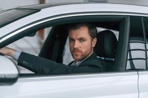 Looking to the side. Man in formal business clothes is sitting in the modern automobile photo