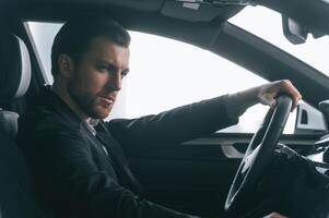 Serious facial expression.. Driving the car. Man in formal business clothes is sitting in the modern automobile photo