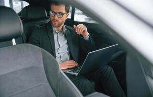 With ,laptop, working. Man in formal business clothes is sitting in the modern automobile photo