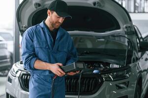 Holding electricity measuring, tool. Man in blue uniform is working in the car service photo