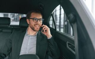 Talking by, phone. Man in formal business clothes is sitting in the modern automobile photo