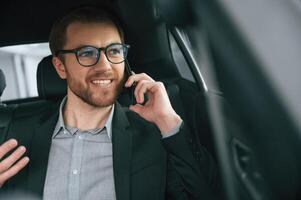 Talking by phone. Man in formal business clothes is sitting in the modern automobile photo