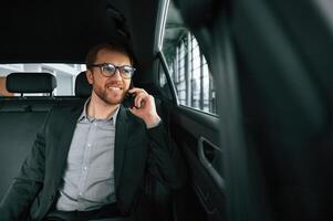 Talking by phone. Man in formal business clothes ,is sitting in the modern automobile photo